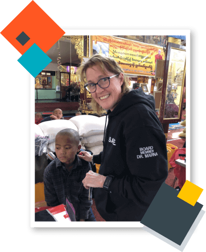 Dr. Marna Geisler wearing black pullover holds a toddler during her peace corps volunteer work.