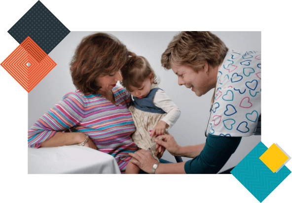 An experienced female pediatrician gives flu shots to a toddler cradled by her mother during a same-day sick appointment. 