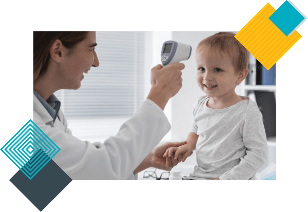 A baby boy smiles sitting on a desk while a pediatrician is checking his temperature using a non-contact digital-thermometer